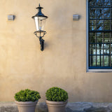 Großer Pflanzkübel Jumbo Bucket Low Classic Taupe als Paar mit immergrünen Sträuchern vor heller Fassade mit Laterne